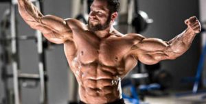 мъжж с мускули, показващ своя бицепс и плочки във фитнес залата